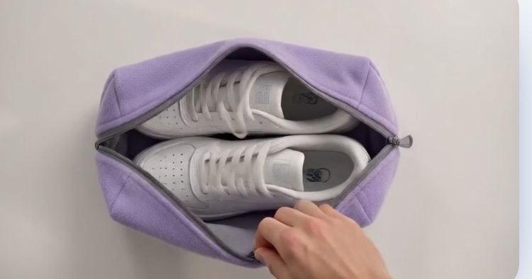 Hand lägger vita sneakers i en lila Washbuddy-påse